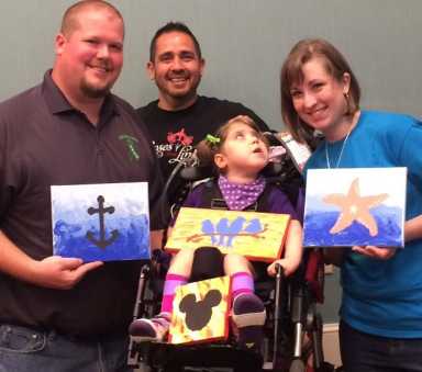 Four-year-old Lily Drake (center) is pictured with her artwork, parents and Roses for Linda founder TJ Hodges.