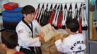 A young child at KOREA Taekwondo breaks a board to symbolize bad habits.