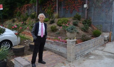 George Negoescu standing beside the garden he created on the corner of Shaler Avenue and Cypress Hills Street in Ridgewood.