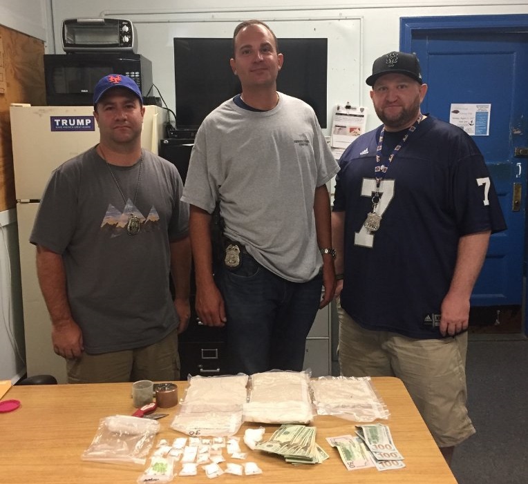 Three 110th Precinct officers are pictured with cash and narcotics seized from a Corona home on July 26.