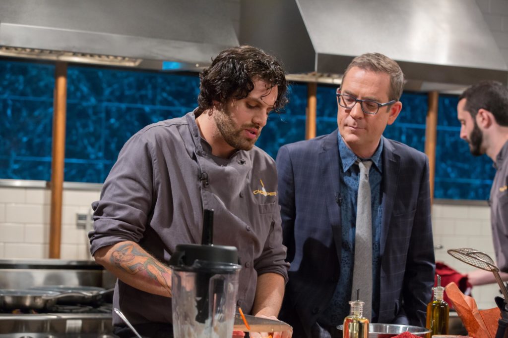 Chef Nick Testa adds olive oil while preparing his second round dish on "Chopped" while Ted Allen looks on.