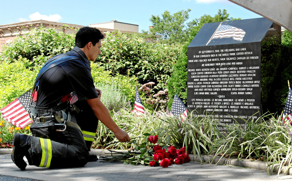 A firefighter lays a flower at the Glendale 9/11 memorial in Dry Harbor Playground