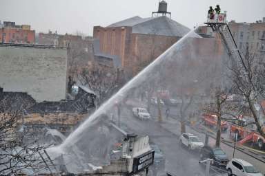 Firefighters use a tower ladder to pour water onto hot spots at the site of a five-alarm blaze in Sunnyside on Dec. 13.