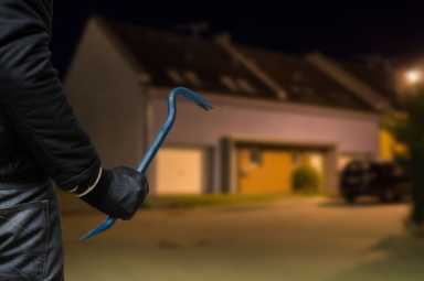 Burglar or robber with crowbar stands in front of house