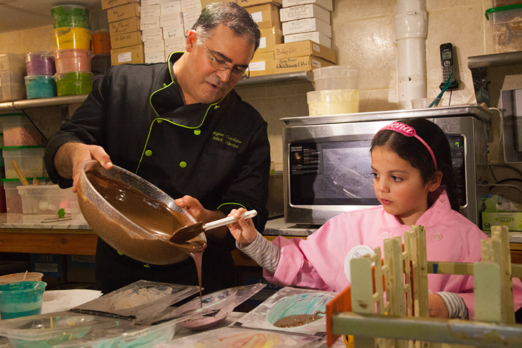Mark Libertini of Aigner Chocolates in Forest Hills shows Athena how to mold chocolate Easter bunnies.