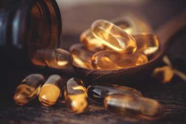 Close up the vitamin D and Omega 3 fish oil capsules supplement on wooden plate for good brain , heart and health eating benefit