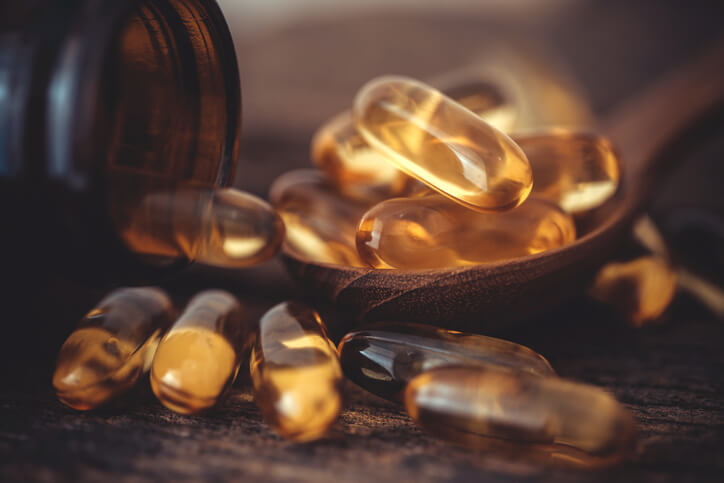 Close up the vitamin D and Omega 3 fish oil capsules supplement on wooden plate for good brain , heart and health eating benefit