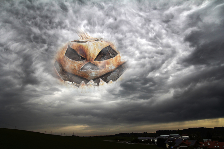 An eerie Halloween pumpkin head in the sky between thunderclouds looks at a city