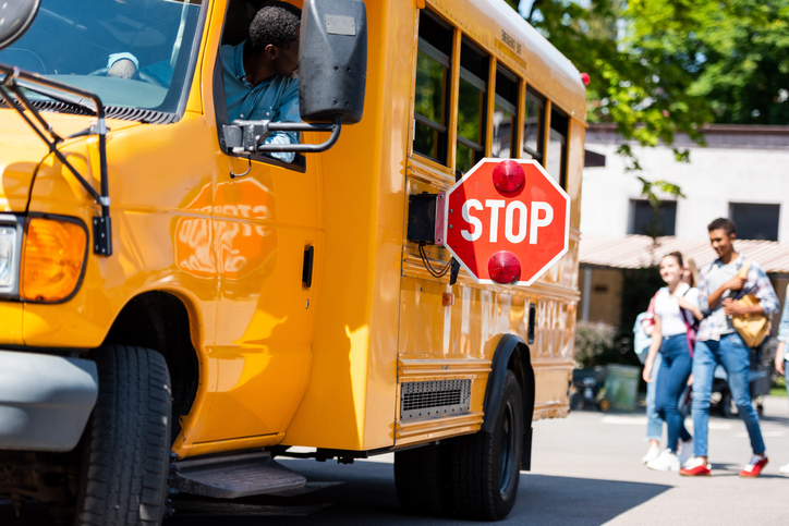 senior school bus driver looking at teens walking behind bus