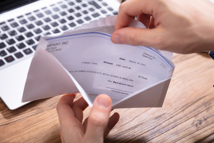 Person’s Hand Removing Paycheck From The Envelope