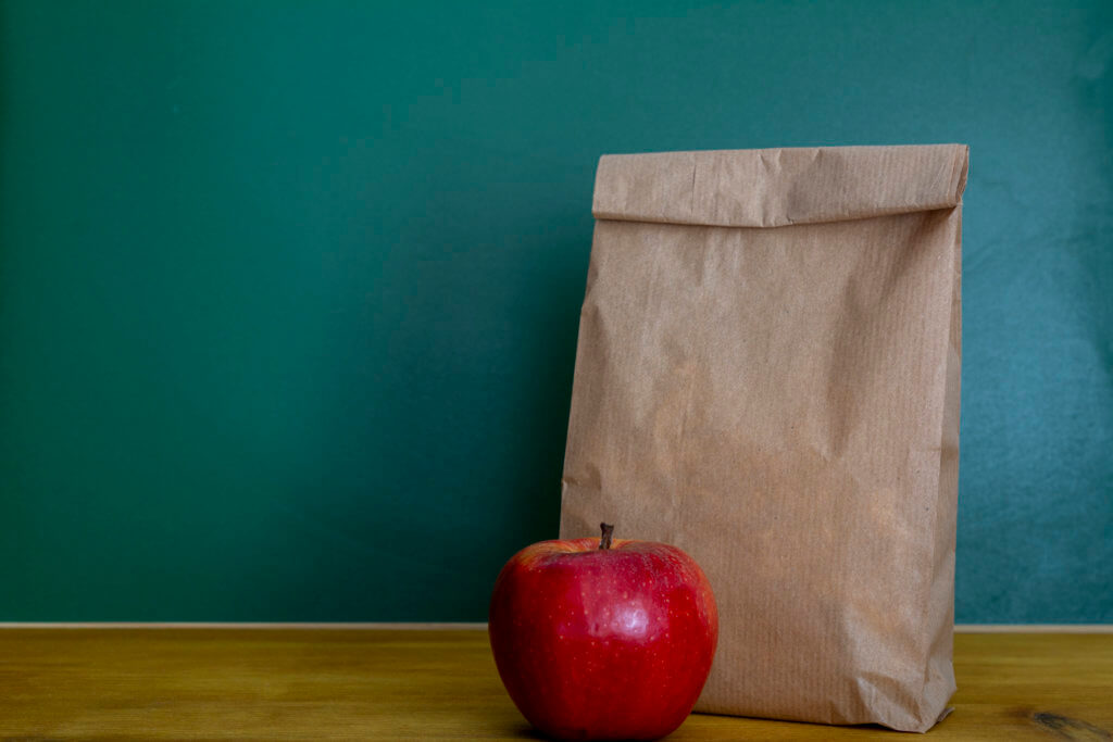 School lunch. Brown paper bag and a red apple on top of wooden desk