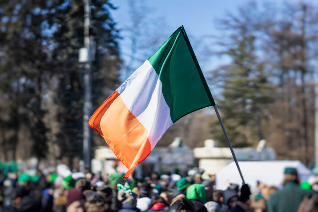 Flag of Ireland close-up in hands on background of blue sky during the celebration of St. Patrick’s Day