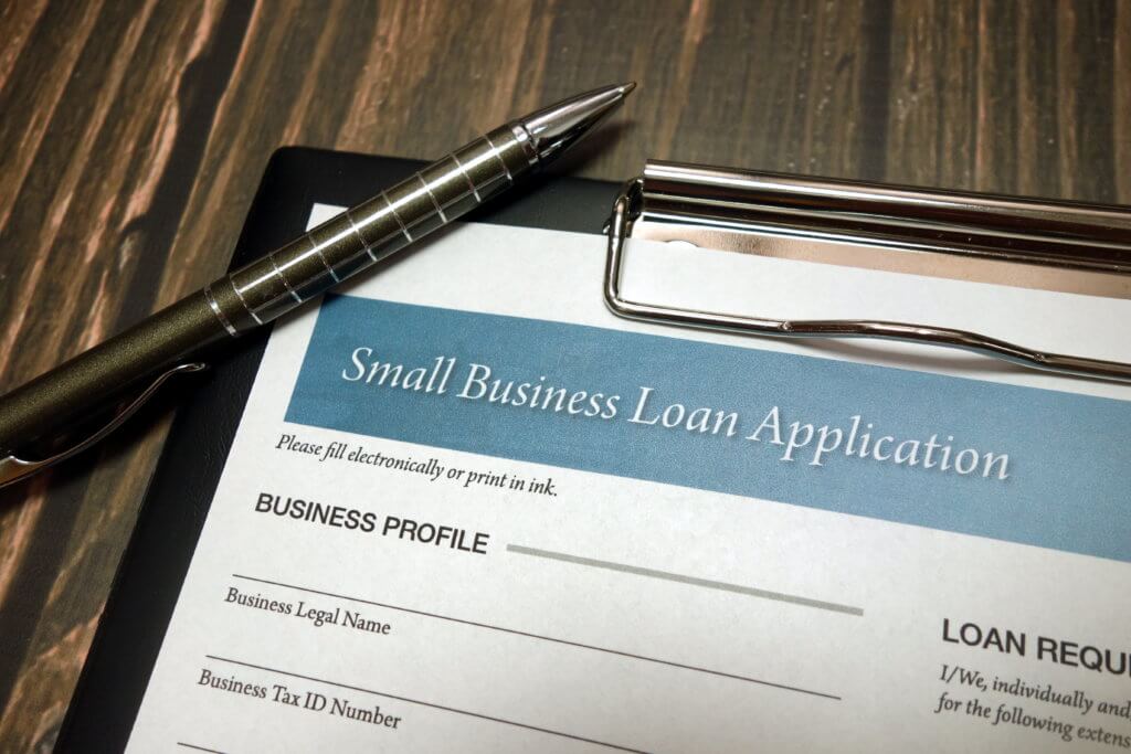 Clipboard with small business loan application form and pen on desk