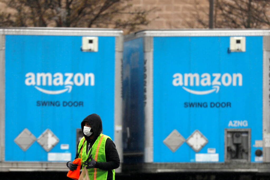FILE PHOTO: A worker in a face mask walks by trucks parked at an Amazon facility as the global coronavirus outbreak continued in Bethpage on Long Island in New York