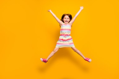 Full size photo of pretty child jumping raising hands isolated over yellow background