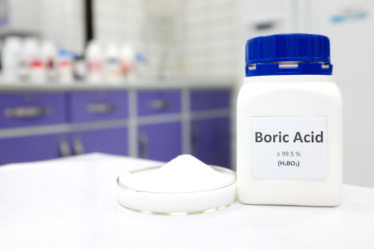 Selective focus of a bottle of pure boric acid chemical compound beside a petri dish with solid crystalline powder substance. White Chemistry laboratory background with copy space.