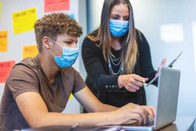 High School Students and Teacher wearing face masks in Classroom Setting working on laptop technology
