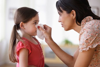 Mother wiping nose of daughter with tissue
