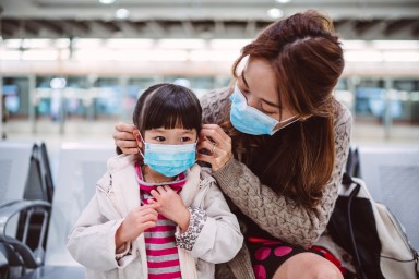 Mom helping her daughter to wear medical face mask on train platform