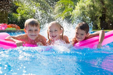 Portrait of three children splashing on inflatable mattress in garden swimming pool
