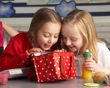 Two little girls peeking into lunch bag in class