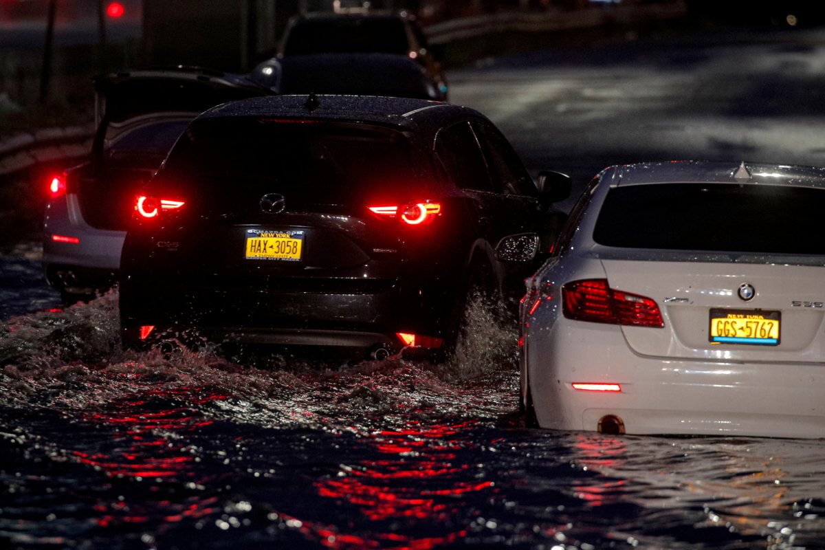 A car navigates past abandoned cars on a flooded highway in Queens, New York
