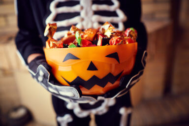 Boy in skeleton costume holding bowl full of candies