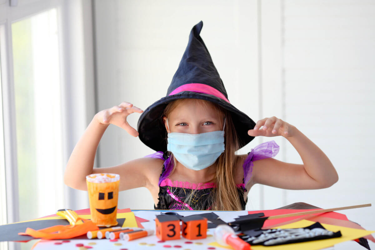 A little girl in a witch costume in a medical mask makes crafts and scares.