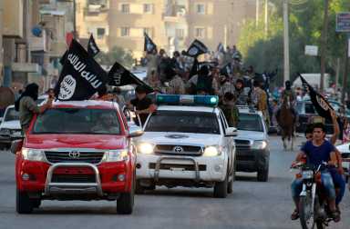 Militant Islamist fighters waving flags, travel in vehicles as they take part in a military parade along streets of Syria’s northern Raqqa province