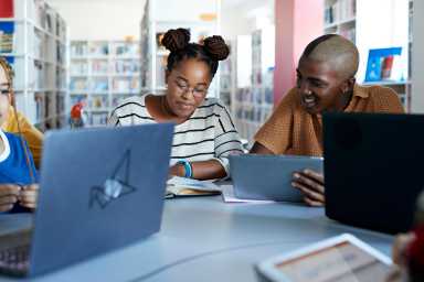 Smiling hipster student with female friend at desk