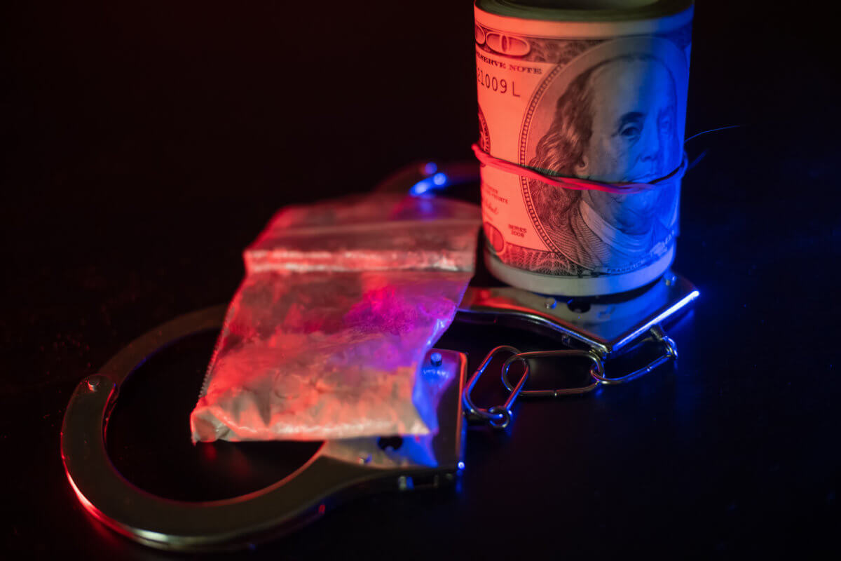 Dollars, handcuffs, drugs on a table in the dark with a red-and-blue police flashing light . Concept of detention, bribes
