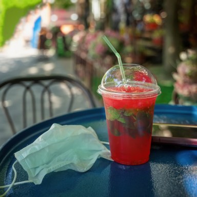 Disposable plastic cup with refreshing drink and protective medical mask, Street cafe table, terrace, summer. New normality, security measures