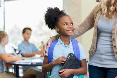 Cute African American schoolgirl talks with teacher before class
