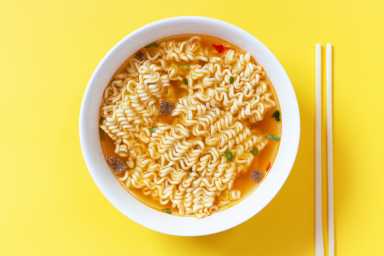 Instant noodle soup in a white bowl on yellow background top view.