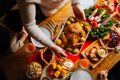 Close-up top view of young father male putting dish with baked hot turkey on holiday dinner table served for Christmas family party