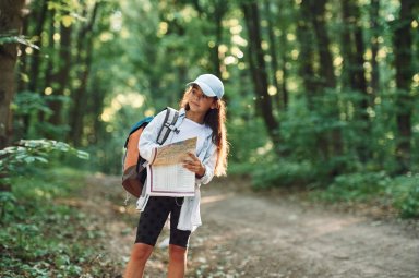 Using the map. Girl is in the forest at summer day time discovering new places