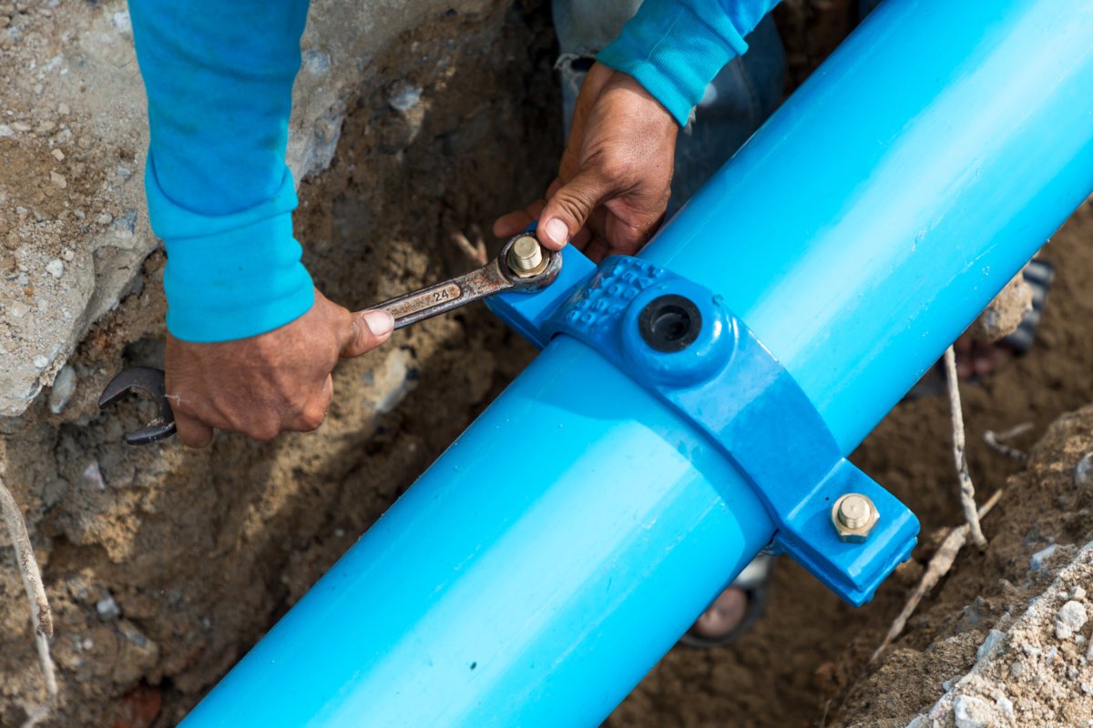 Man using a large wrench on water pipes. Construction site with new Water Pipes in the ground. Sewer pipes to repair or restore in street city.