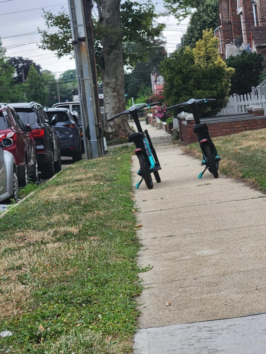 Two parallel e-scooters block the pathway of a sidewalk.