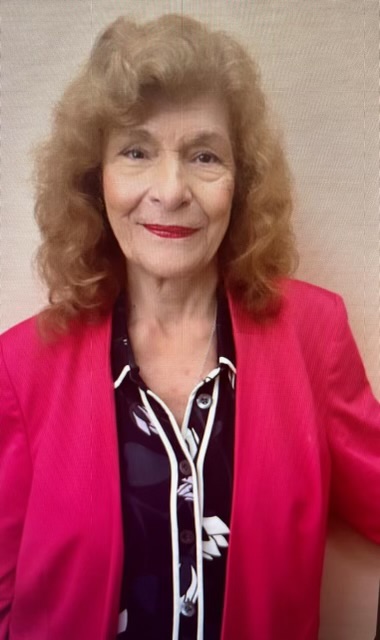 A senior woman in a hot pink blazer smiling in the camera.