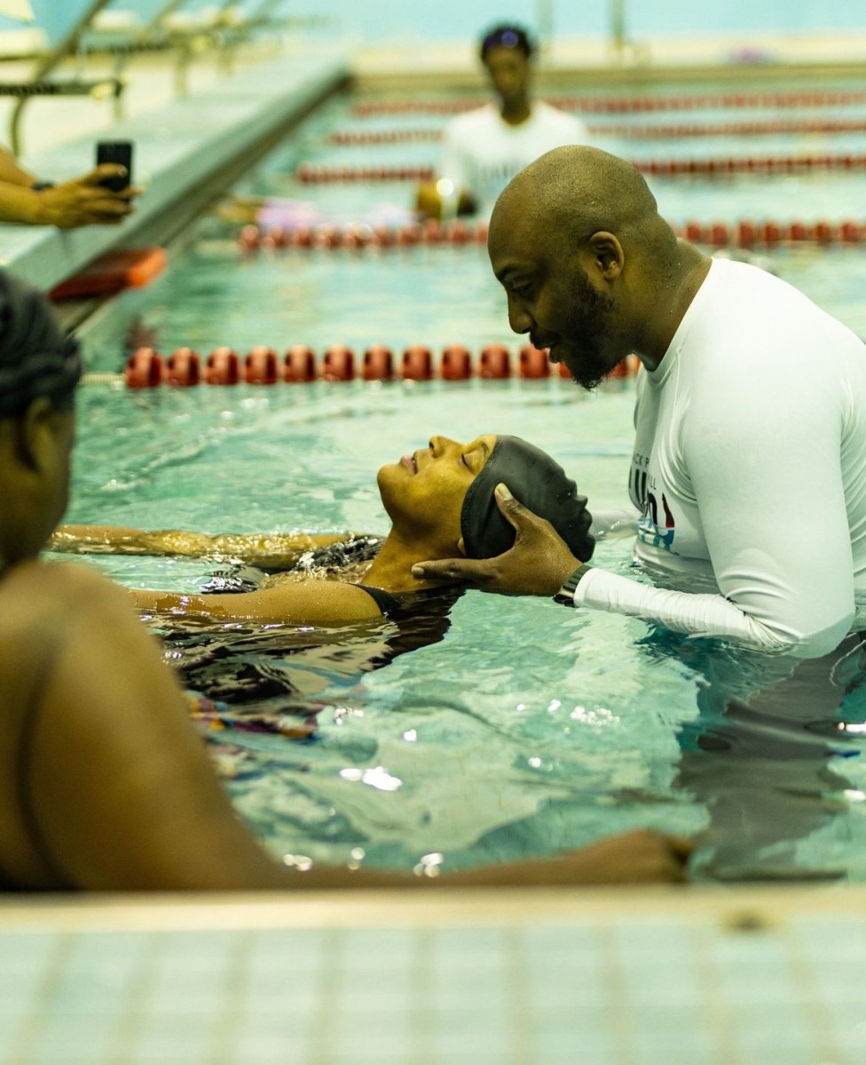 Male swim instructor holds woman's head forward as she floats on her back