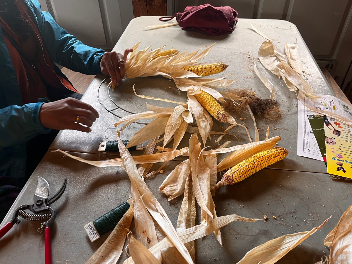 A woman makes a wreath out of the leaves from ears of corn.