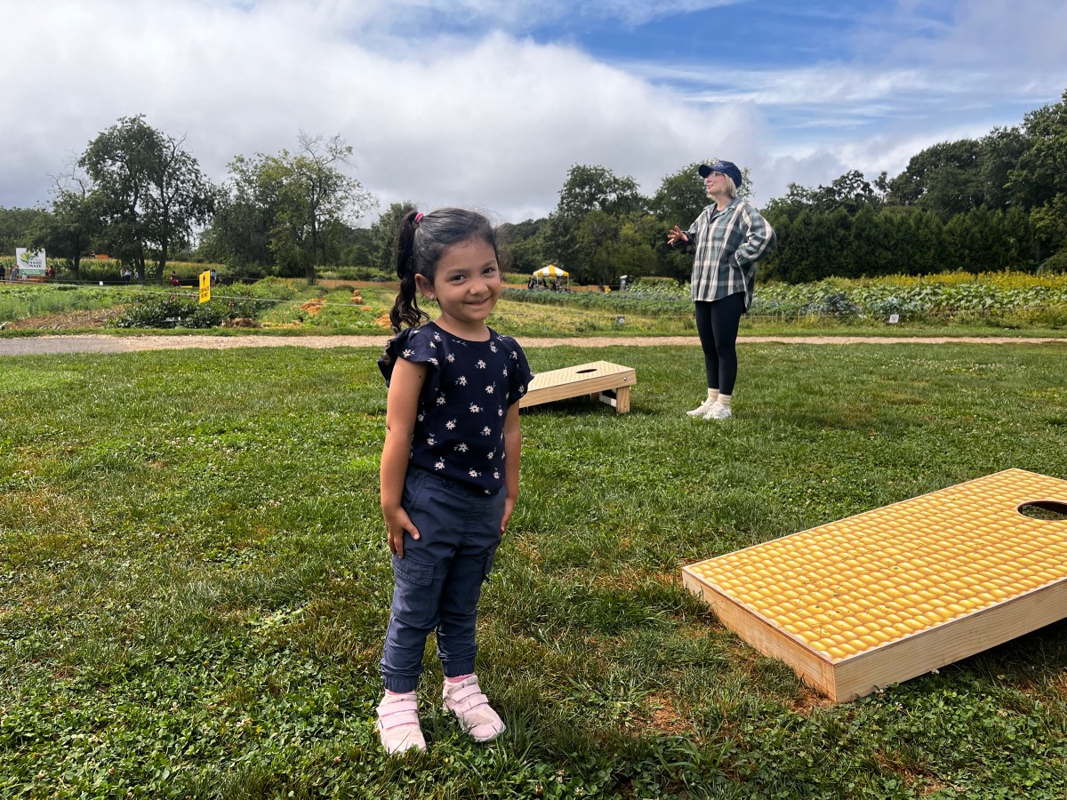 Little girl stands next to corn-hole game board.