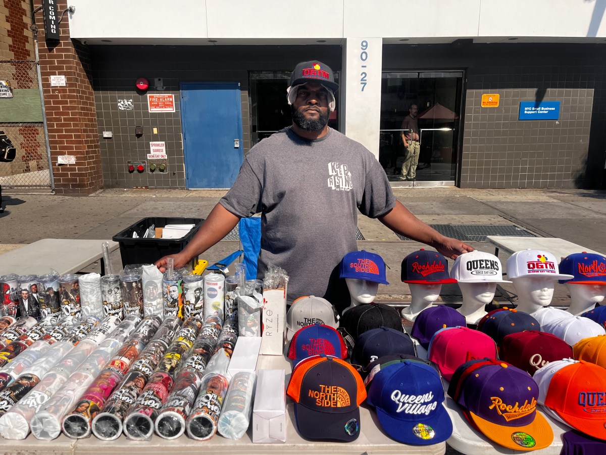 Man stands behind table full of snap-back hats and tumblers.