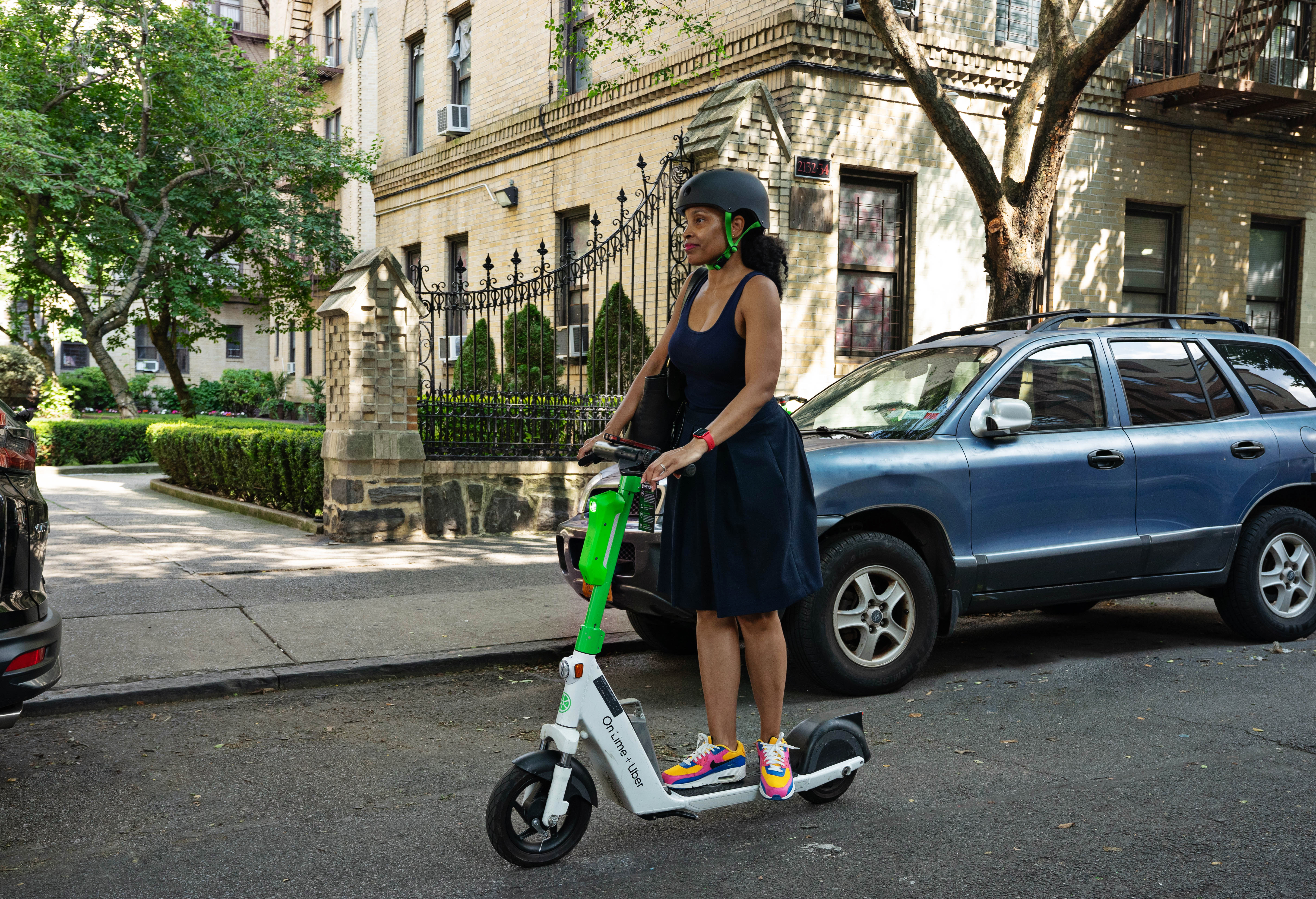 A Black woman in a black dress rides a Lime e-scooter with a helmet on