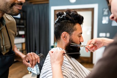 Barber trimming a customer’s beard at a barber shop, small business