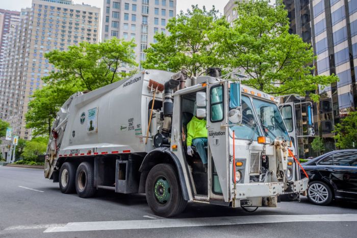 A garbage truck driving around the almost empty streets of