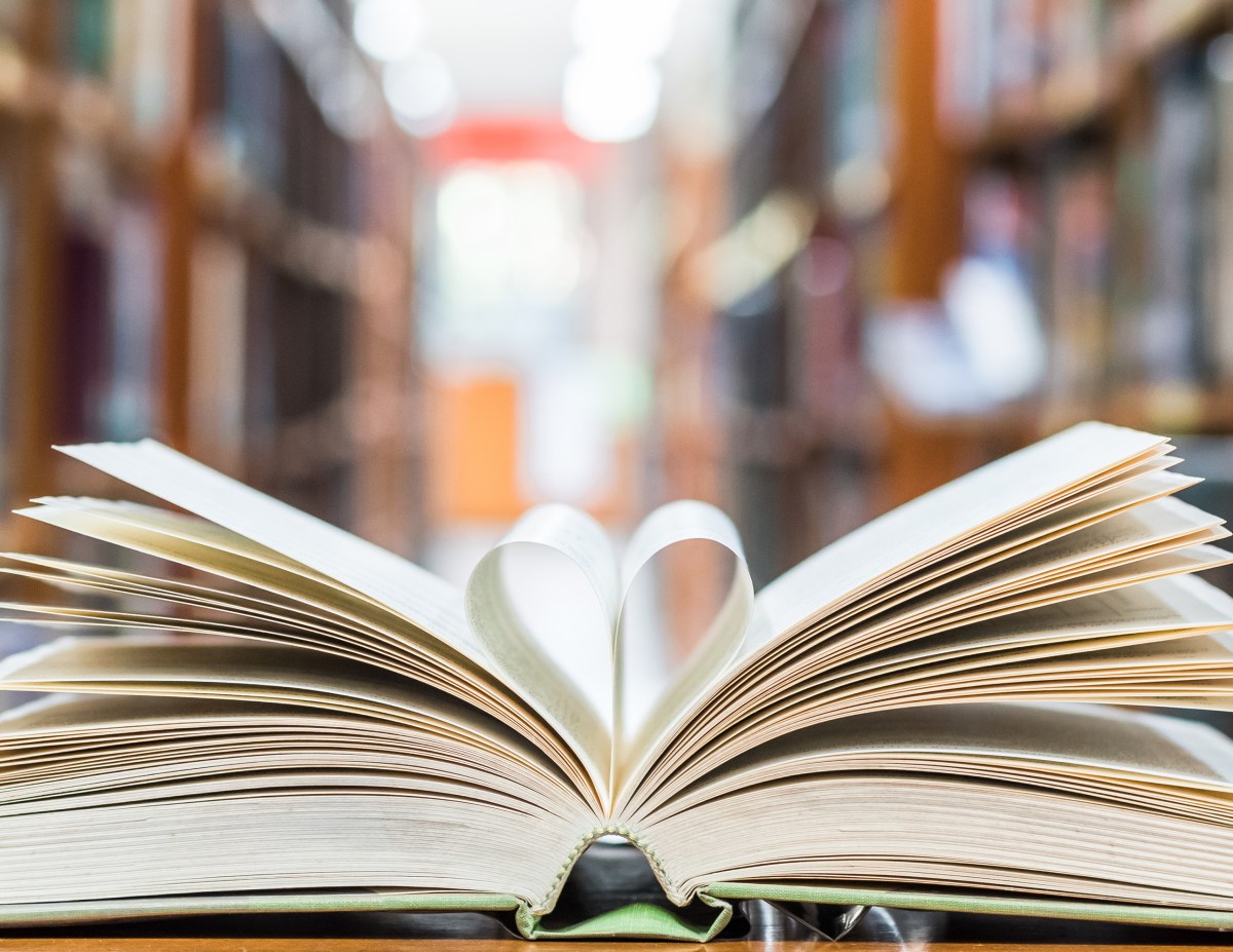 Love story book with open page of literature in heart shape and stack piles of textbooks on reading desk in library, school study room for national library lovers month  and education learning concept