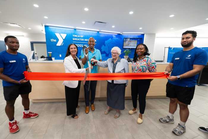 Staff members hold a ribbon being cut by Interim Executive Director of the Cross Island YMCA Tiffany Dunbar, Assemblymember Clyde Vanel and State Senator Toby Ann Stavisky. Also pictured is Board Chair Nadia Cadogan.