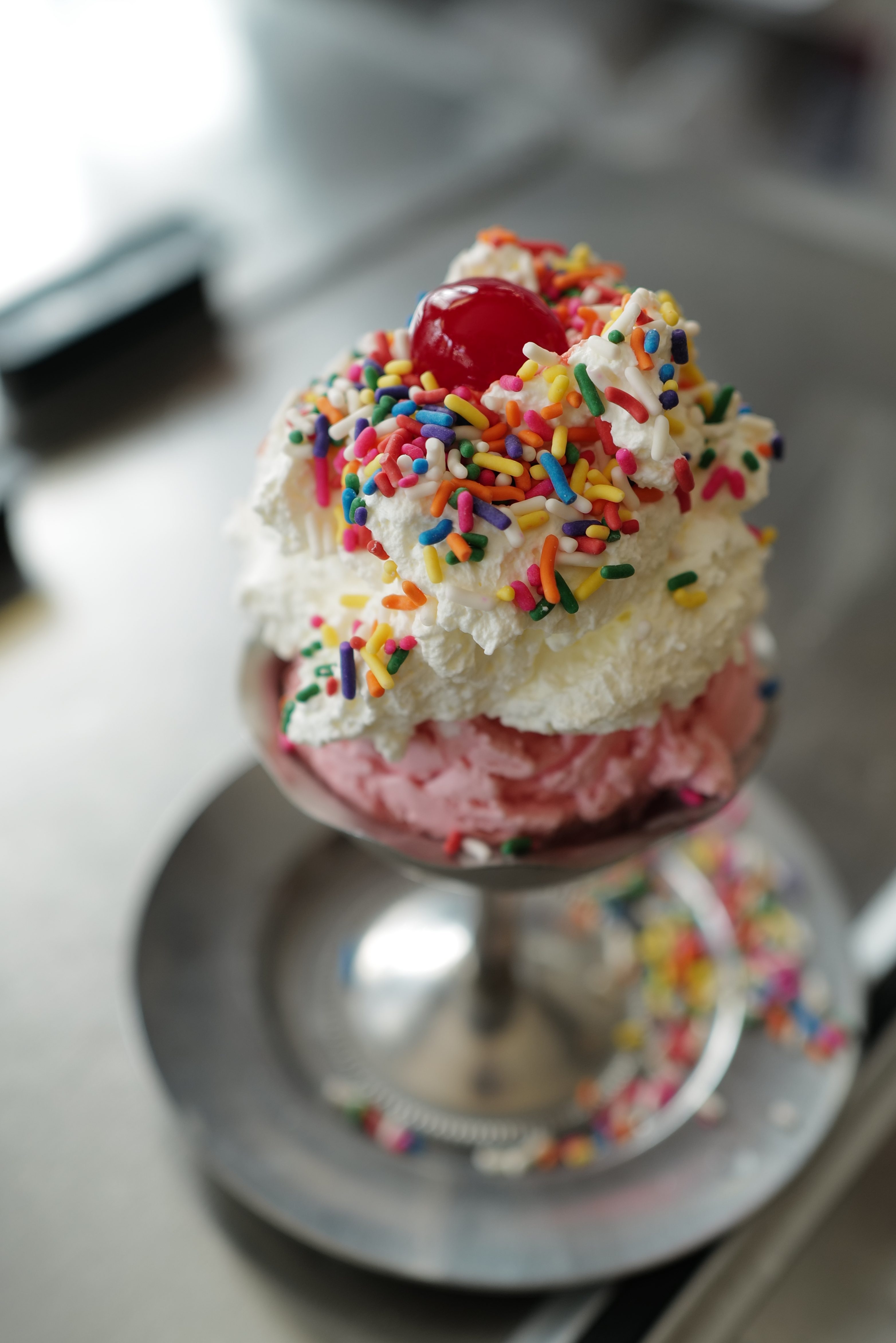 A scoop of strawberry ice cream, topped with whipped cream, rainbow sprinkles and a cherry, at Eddie's Sweet Shop in Forest Hills.
