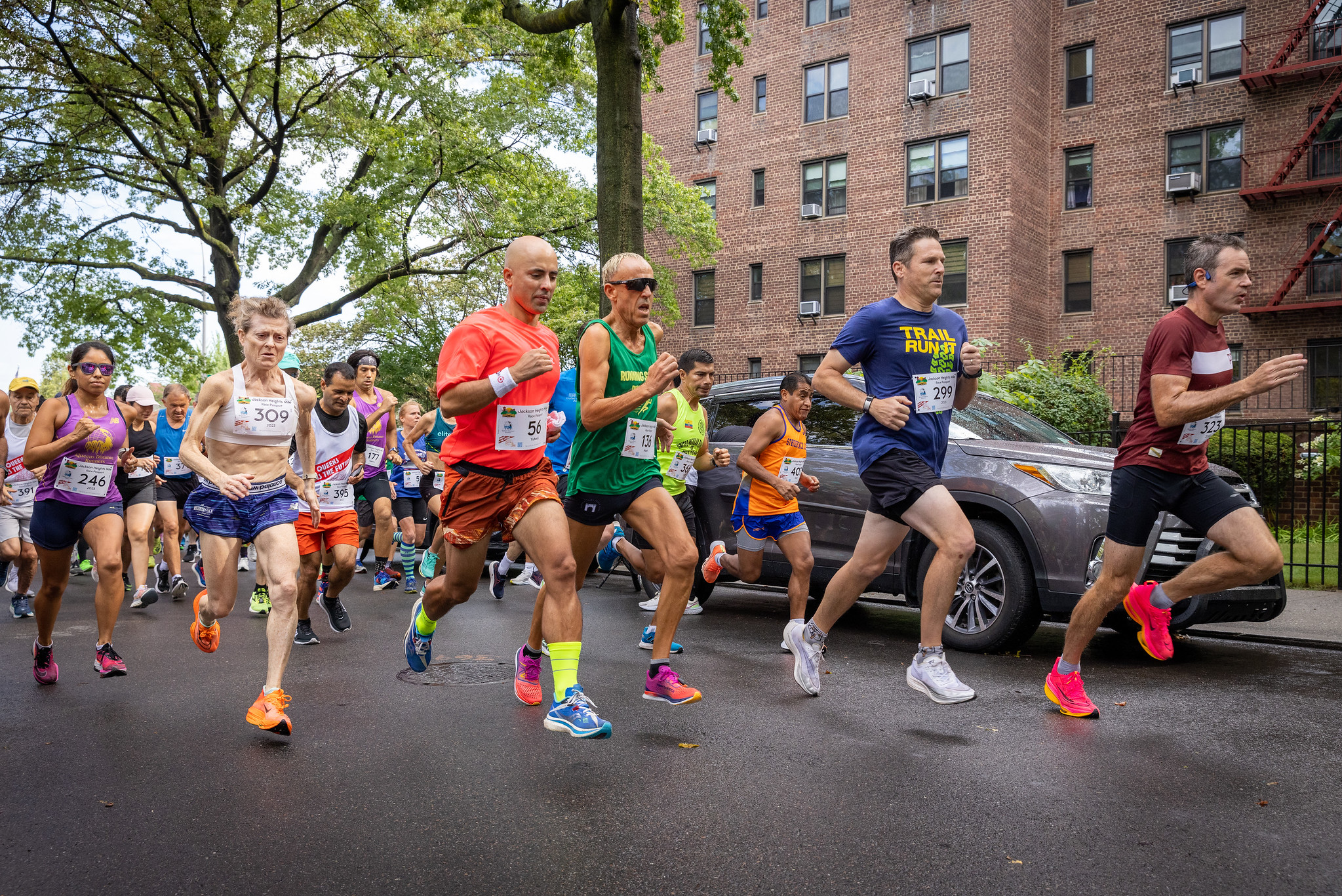 A crowd of runners sprinting towards 34th Avenue at the 2023 QDR Jackson Heights.